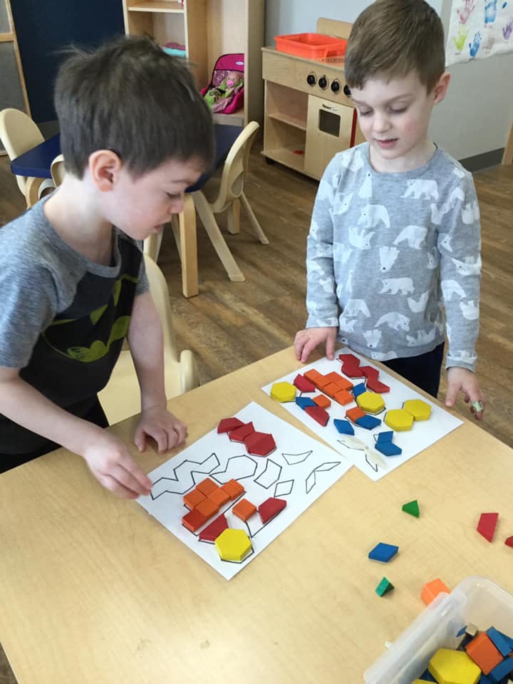 Two children playing with colorful geometric shapes on paper at a table