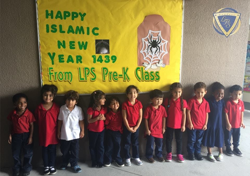 Children standing in a line in front of a banner that reads "Happy Islamic New Year 1439"