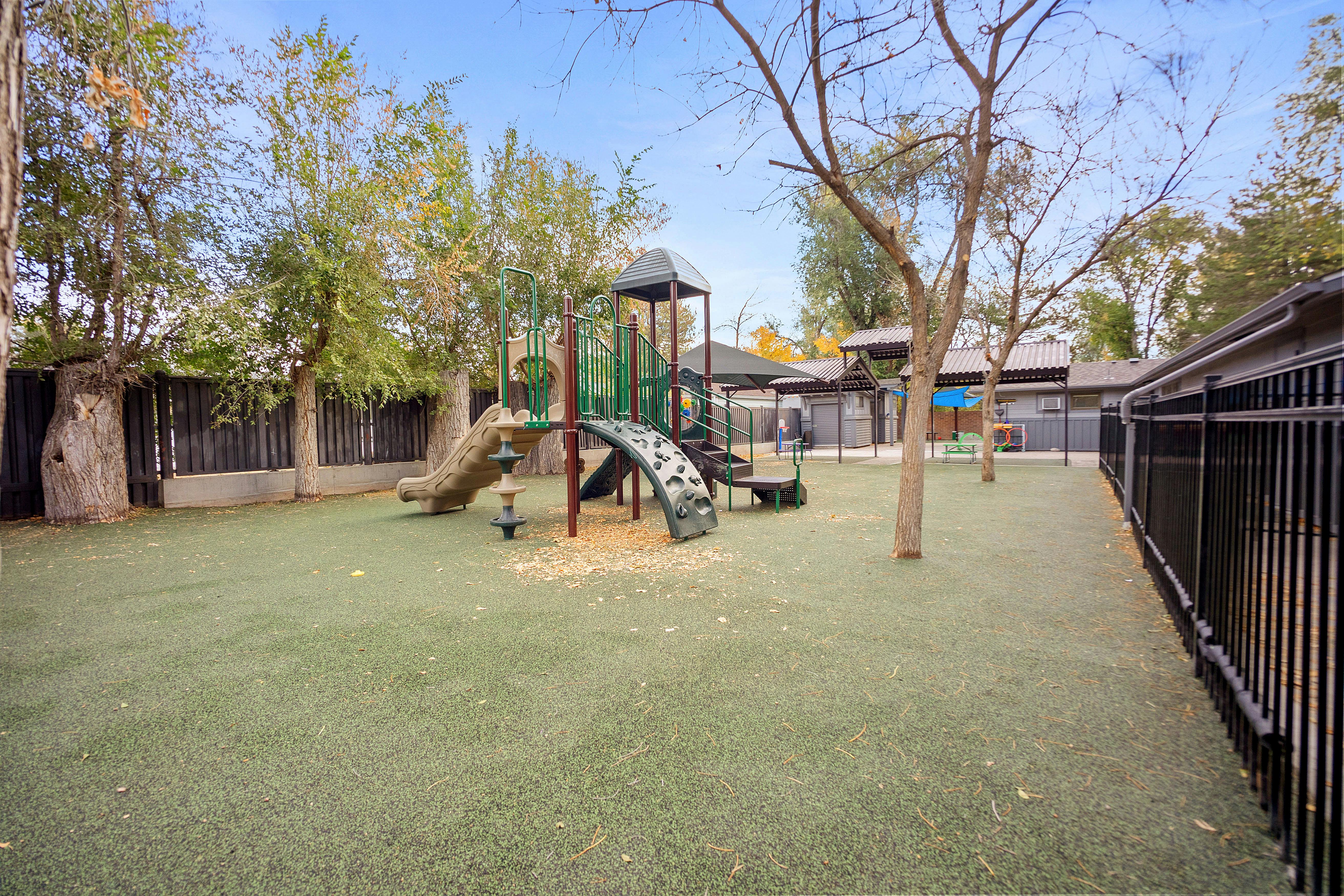 Playground with a green and brown slide and climbing structure on artificial turf