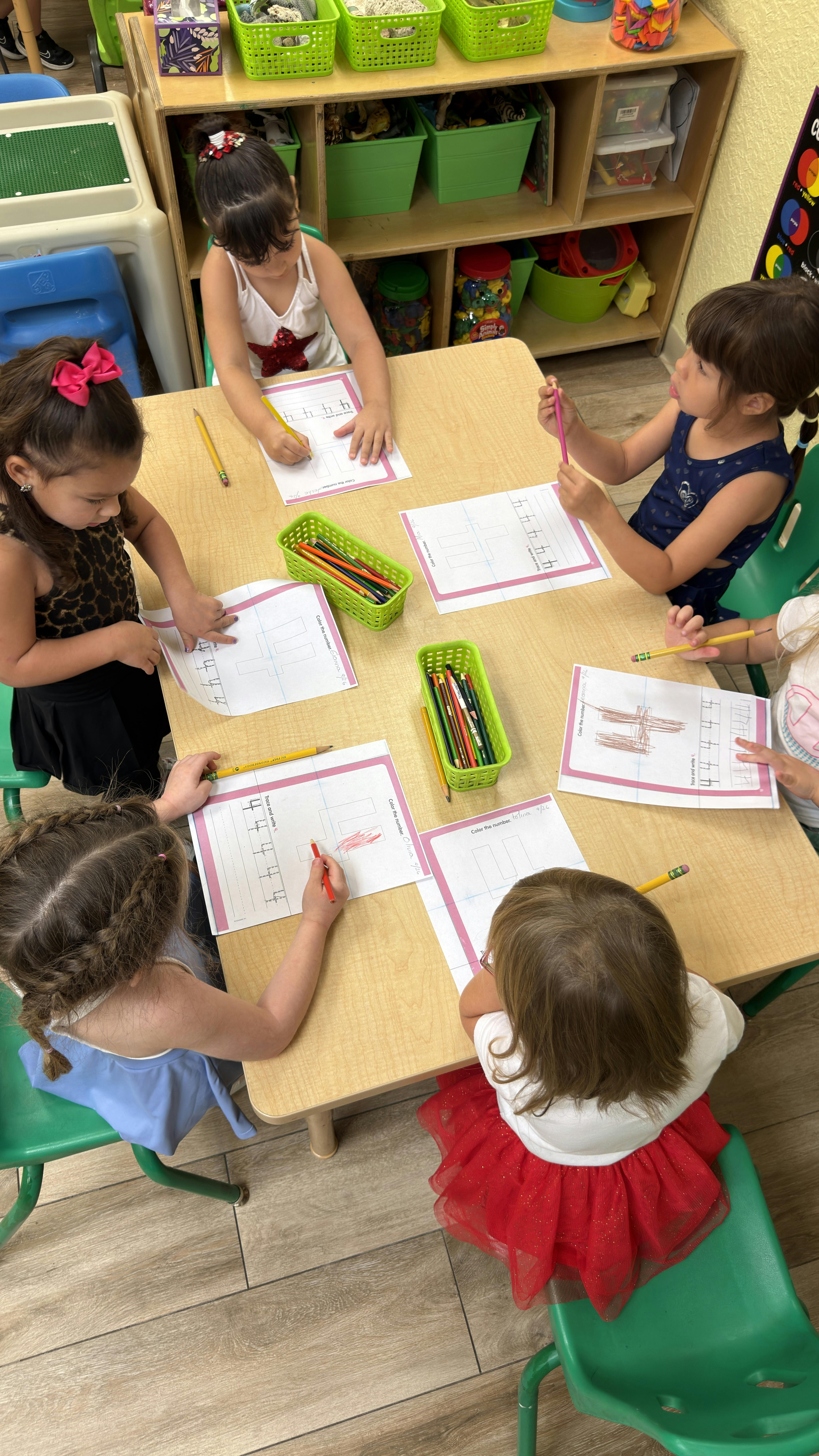 Children working on number writing practice worksheets at a classroom table