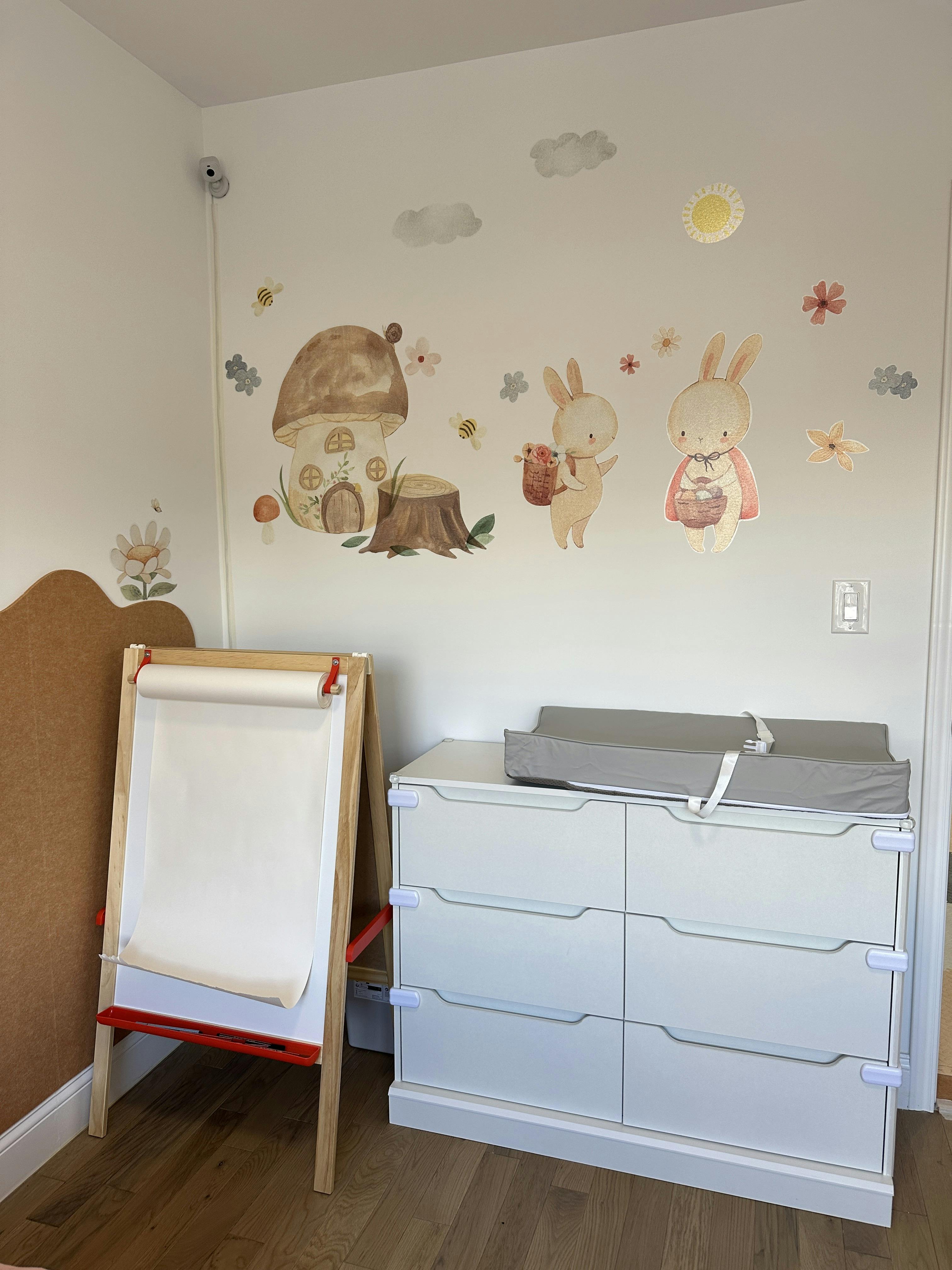 Wall decals of bunnies and a mushroom house above a changing table and easel