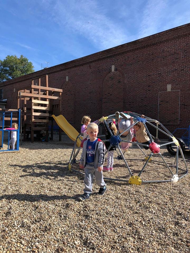 Child walking on wood chips with other children on playground equipment