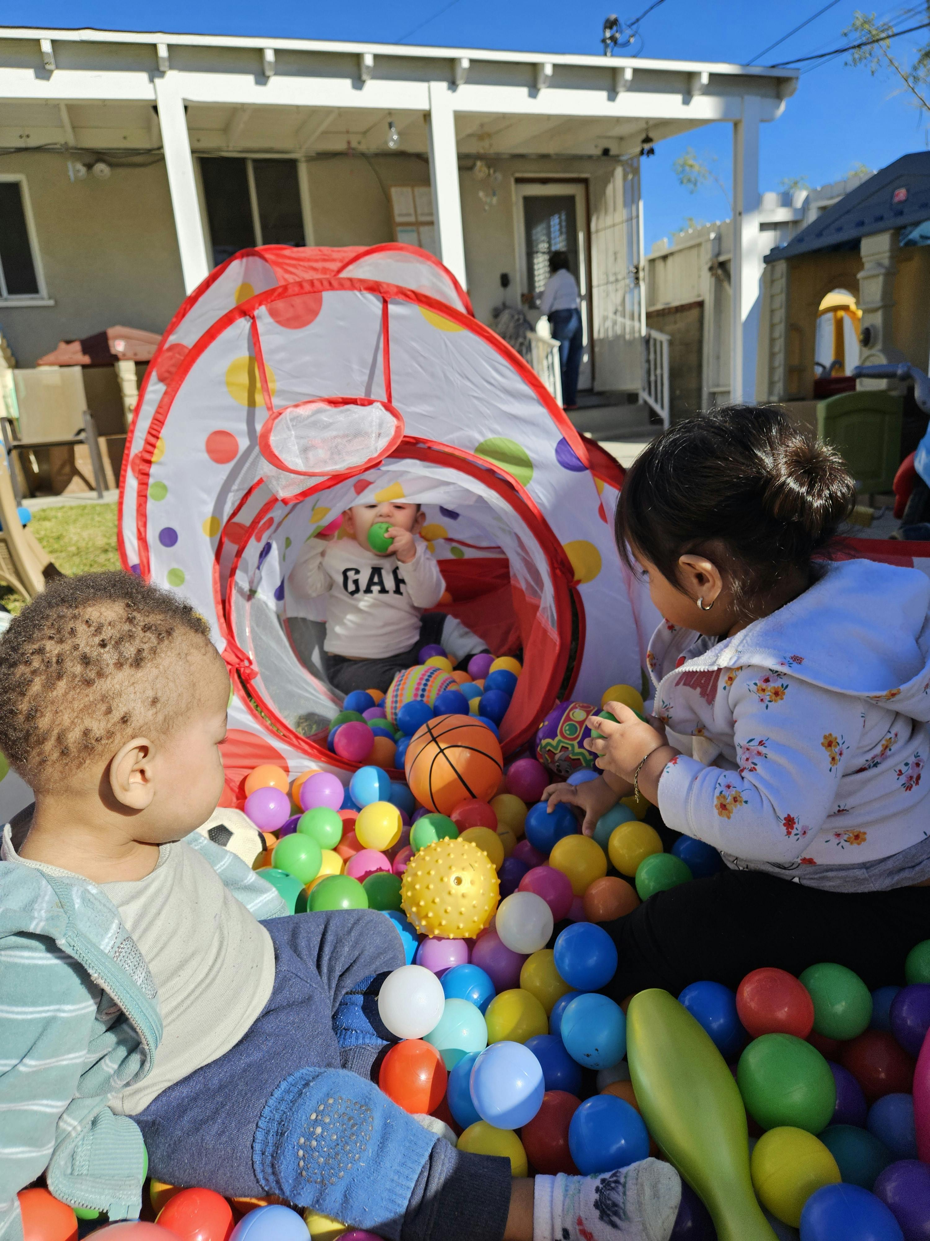 Three children playing in a ball pit and a tunnel