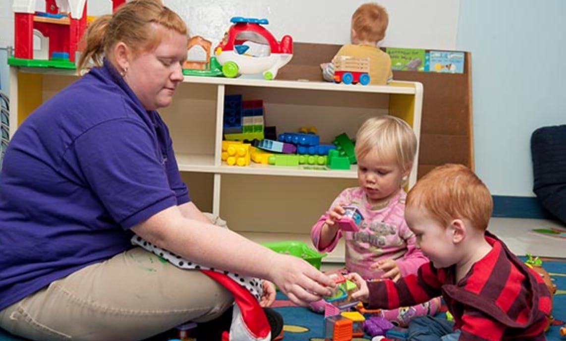 Person playing with two children in a classroom
