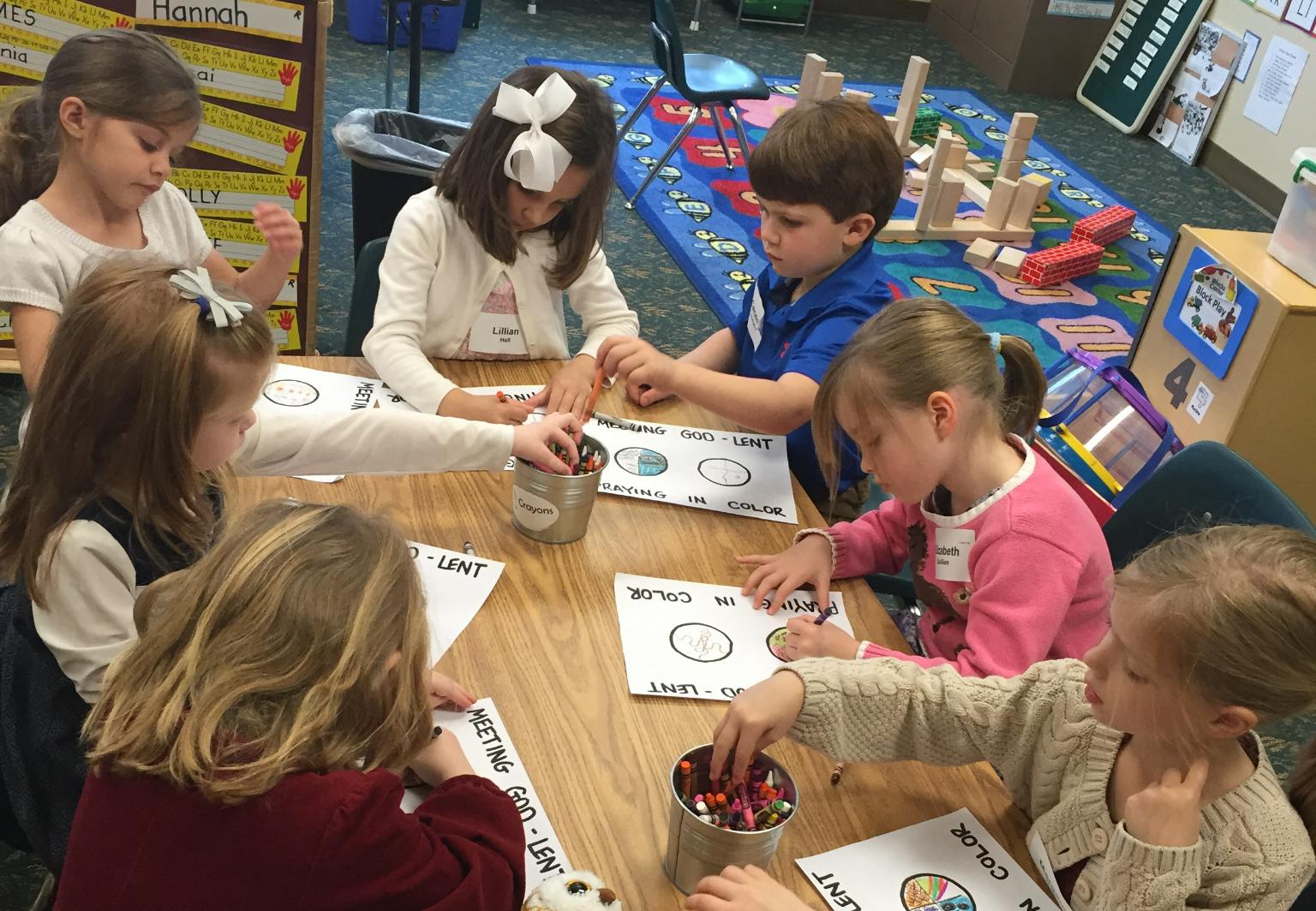 Children sitting at a table coloring worksheets in a classroom