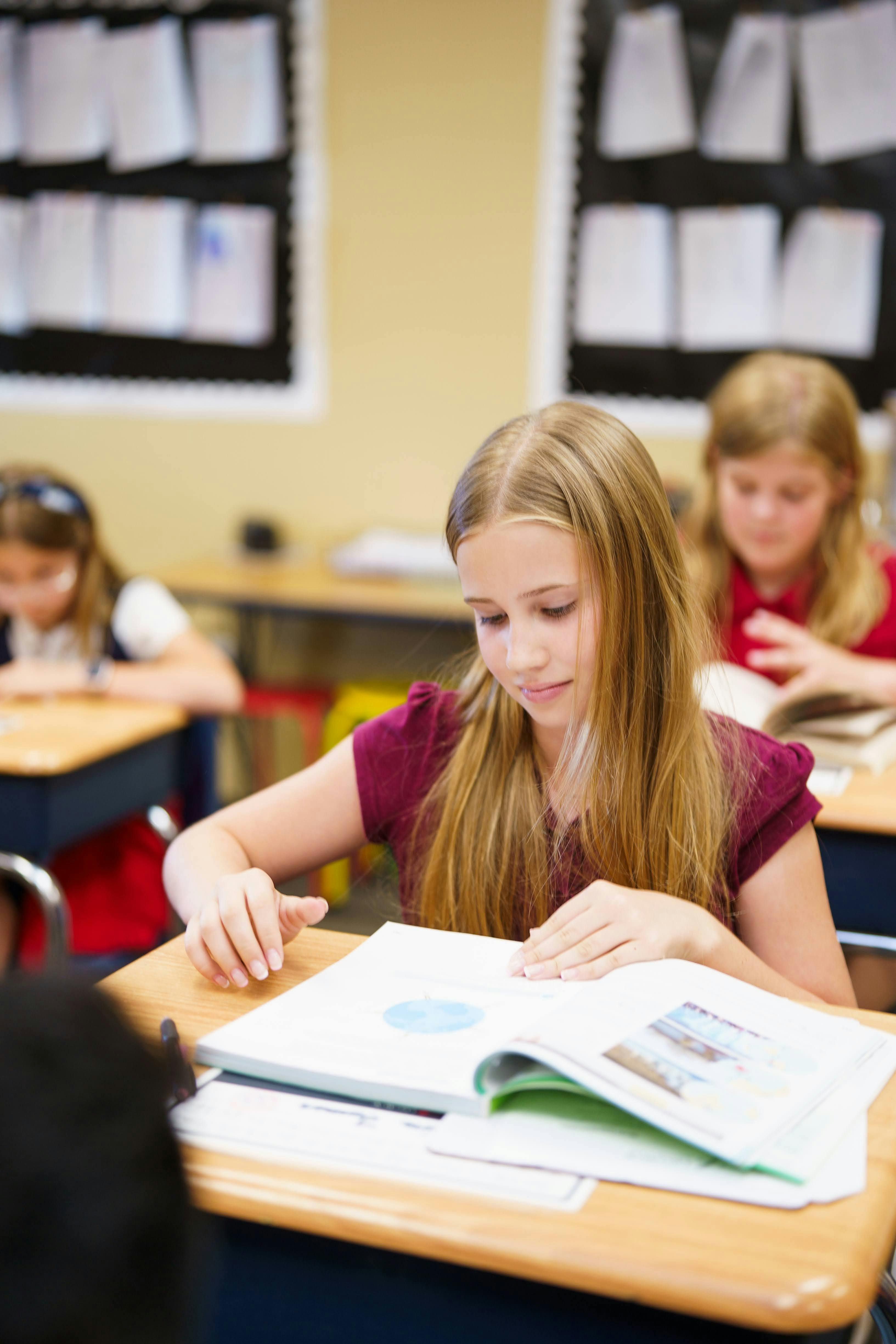 Child reading a book at a desk in a classroom