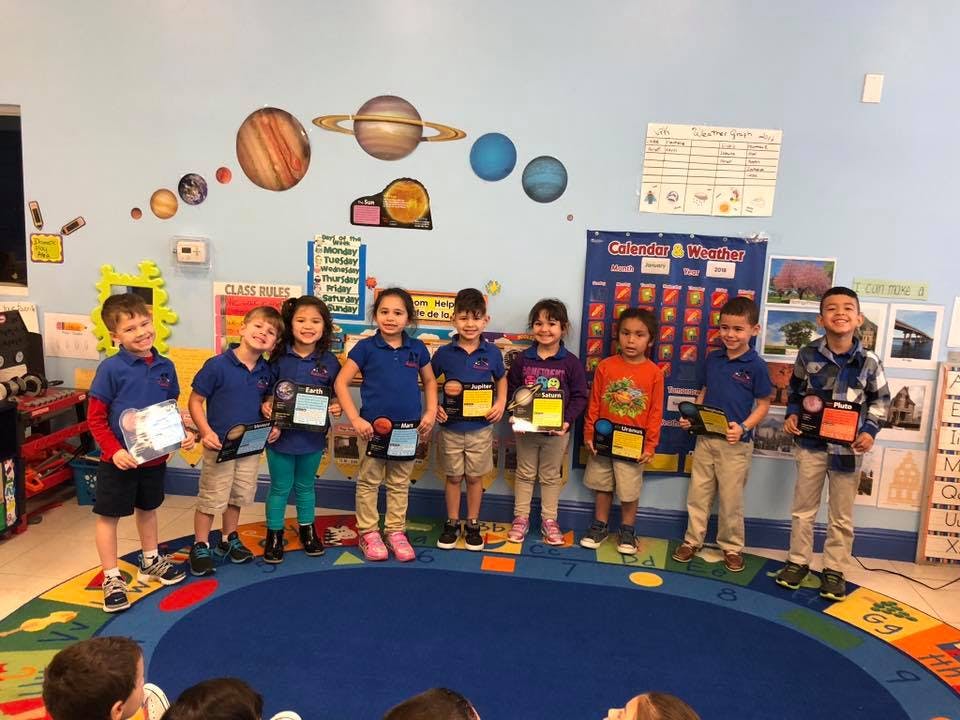 Group of children standing in a classroom with awards