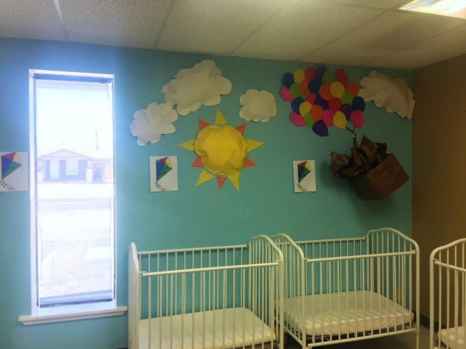 Nursery room with cribs and wall decorations of sun, clouds, and balloons