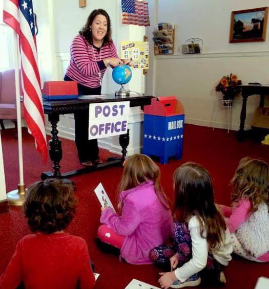 Person teaching children about a globe in a classroom with a "Post Office" sign