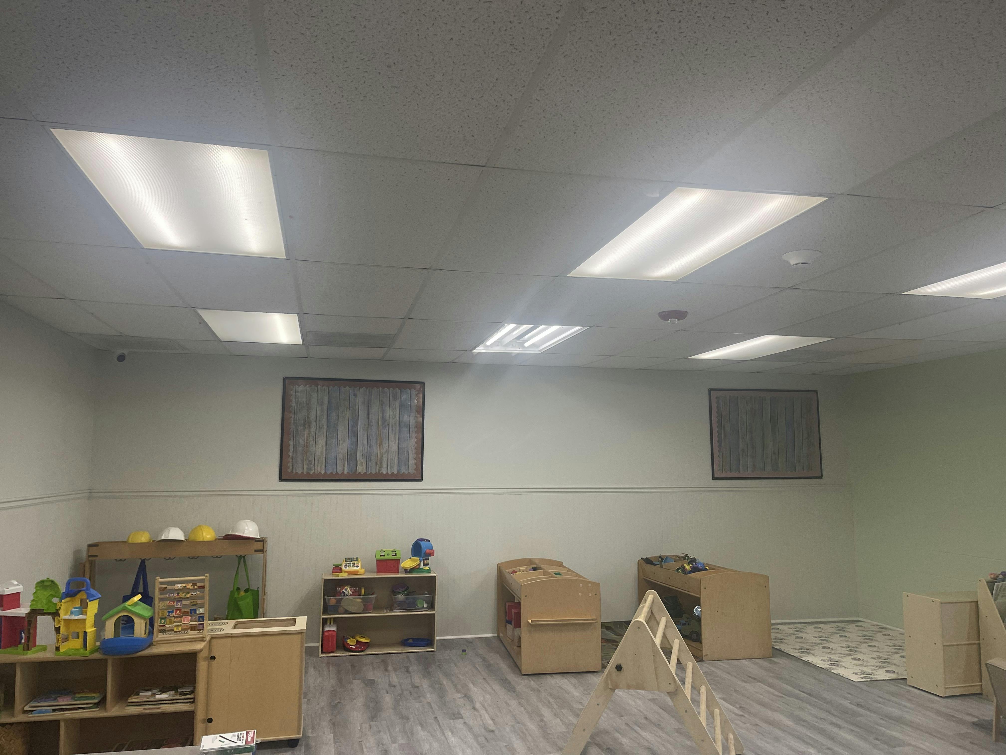 An empty classroom with various toys, wooden shelves, and cots on a gray floor
