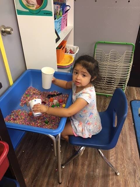 Child playing with cups and colorful beads at a blue table