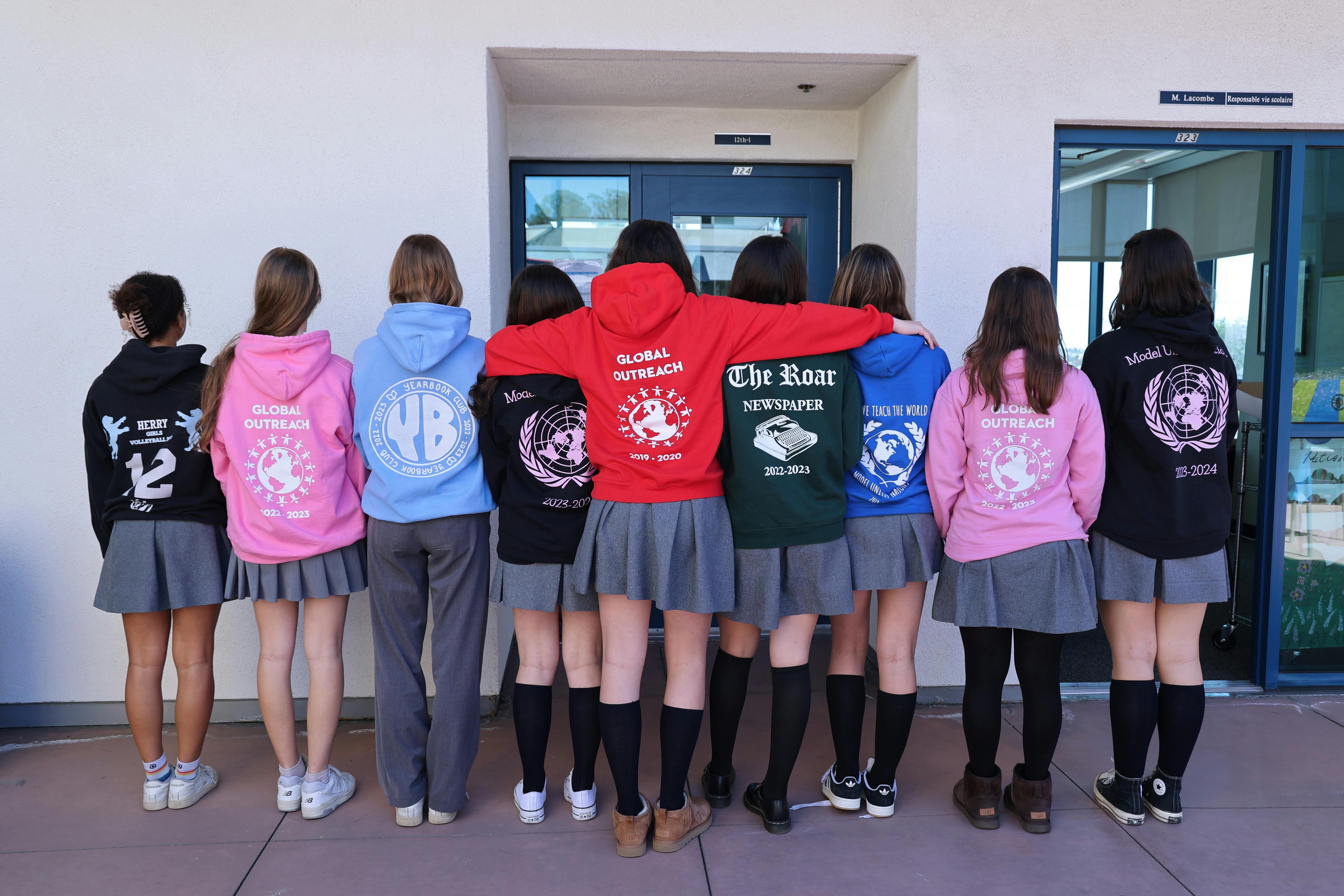 Group of teens in hoodies and skirts standing with backs to viewer