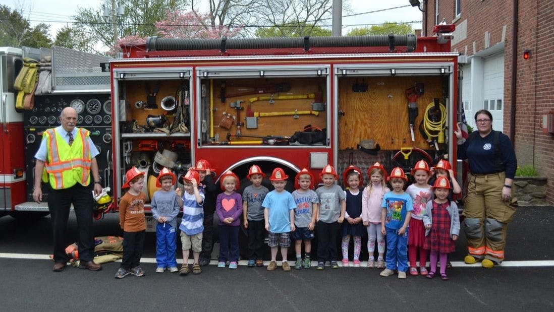 Two adults and multiple children in front of a fire truck