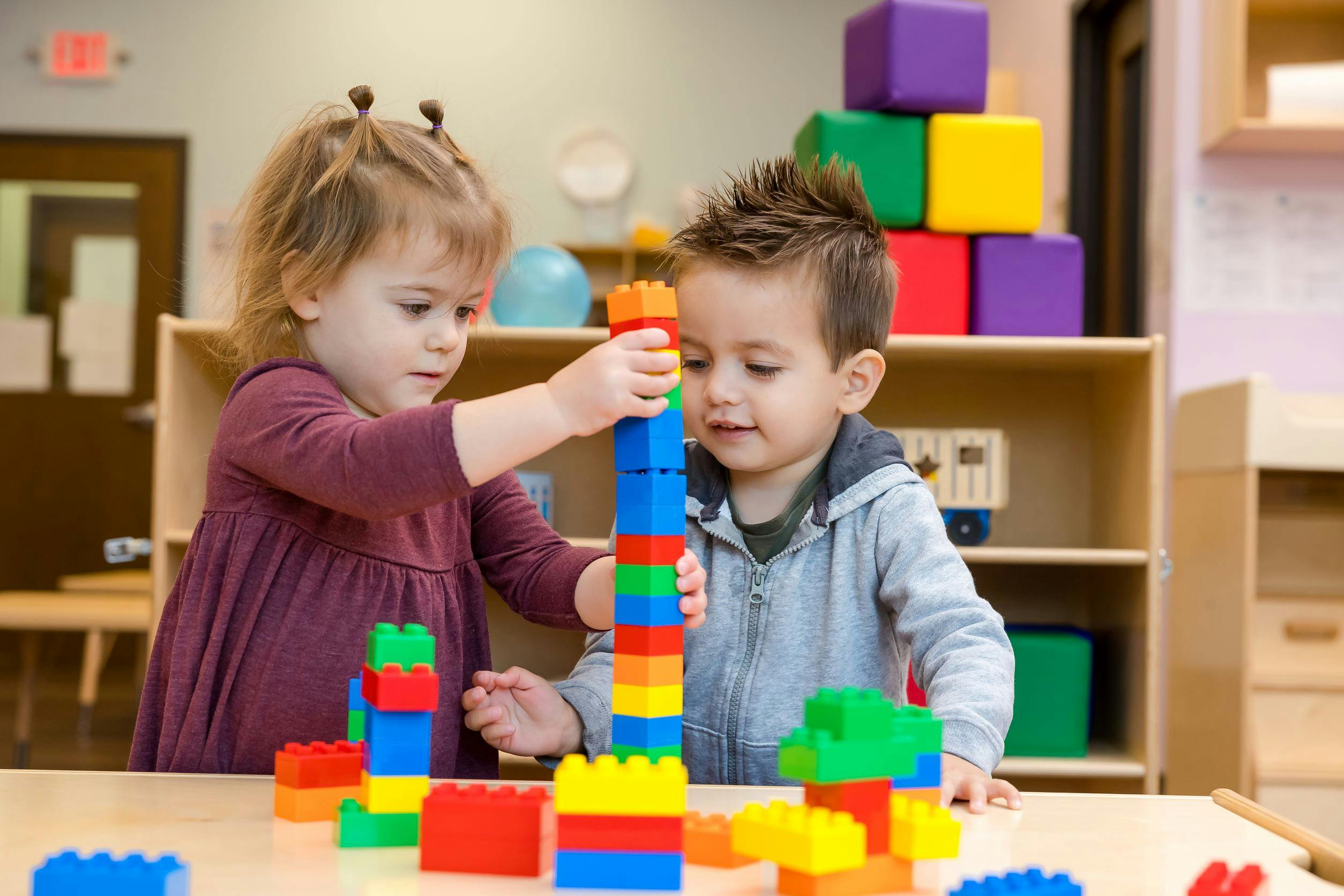 Two children building a tall tower with colorful interlocking blocks
