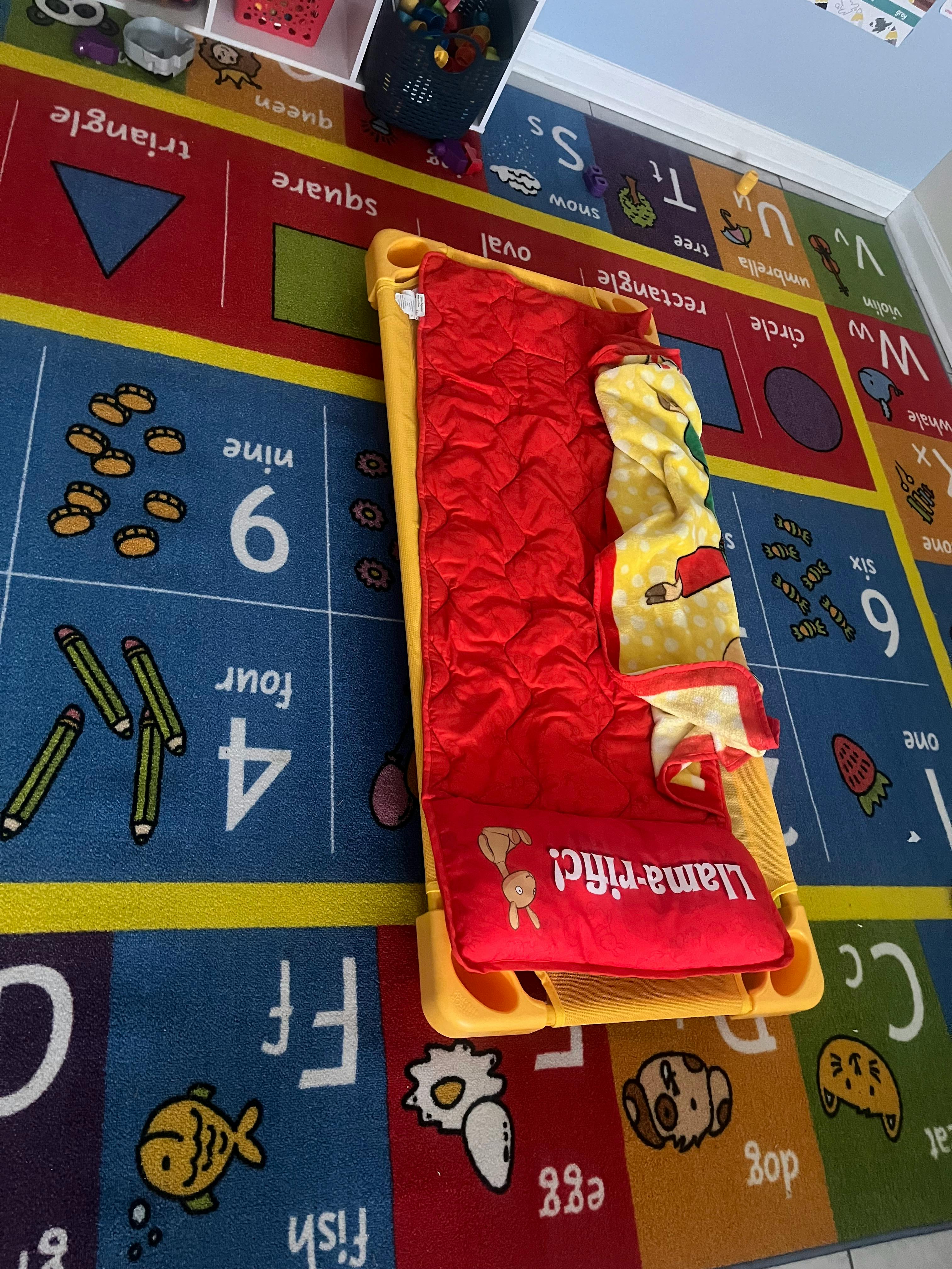 Child's cot with red bedding on a colorful alphabet and number rug