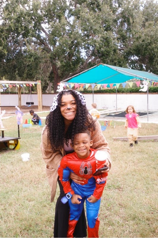 Person holding a child in a superhero costume outdoors