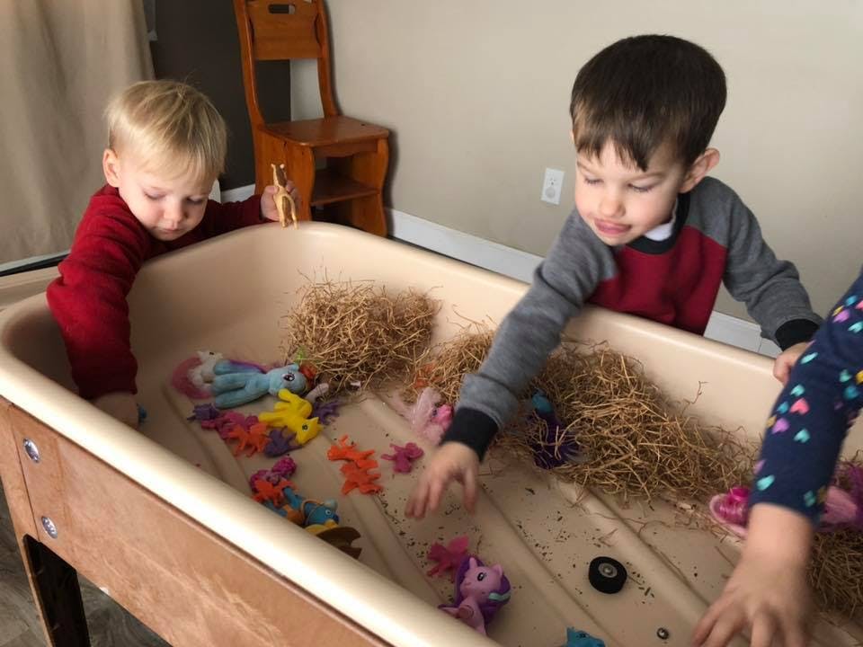 Two children playing with toys in a sensory bin