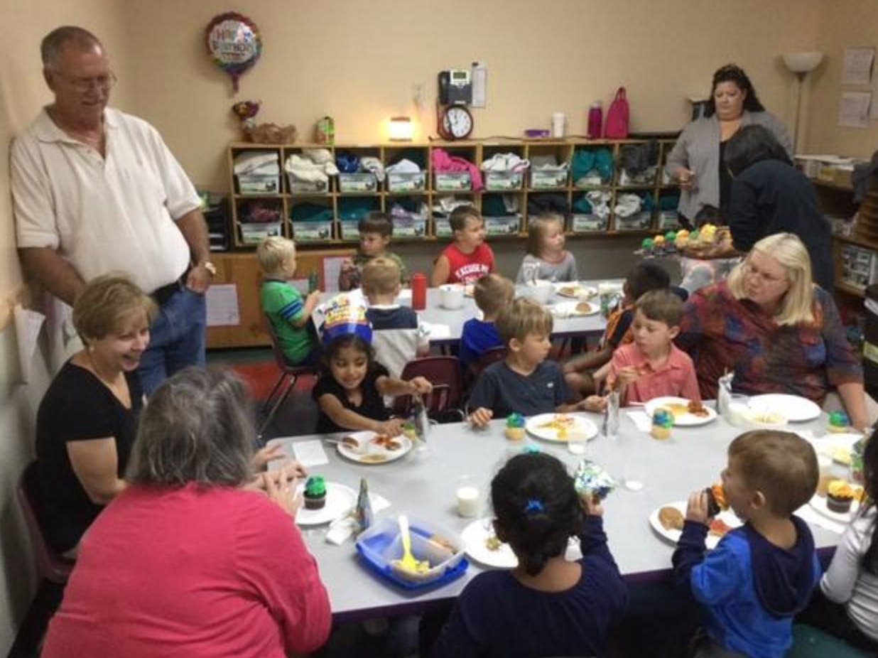 Adults and children eating at tables in a classroom