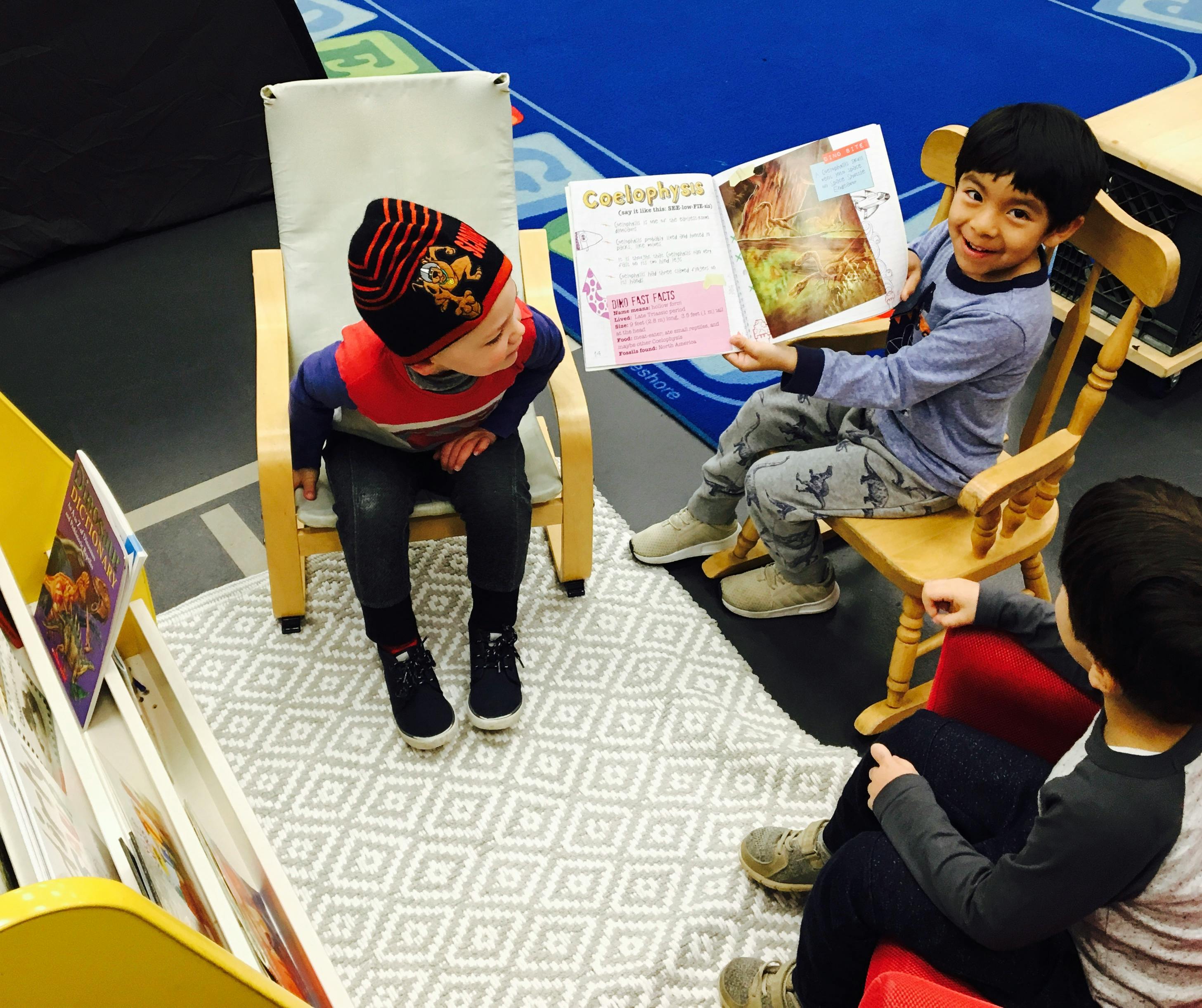 Child reading a book to two other children in a classroom