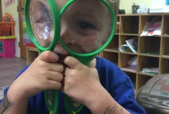 Child holding two green magnifying glasses in front of face