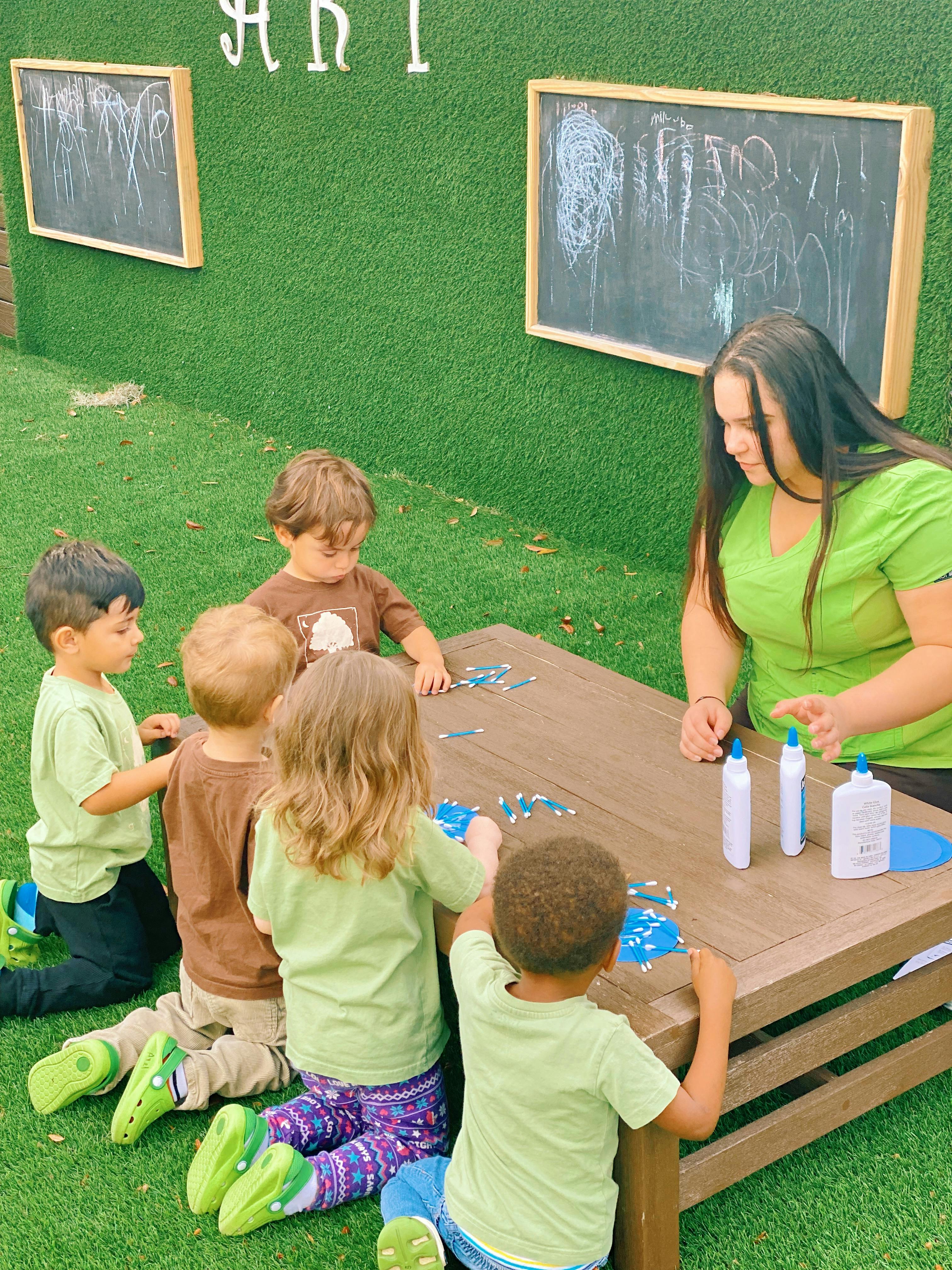 Adult and children doing an art activity at a table outdoors