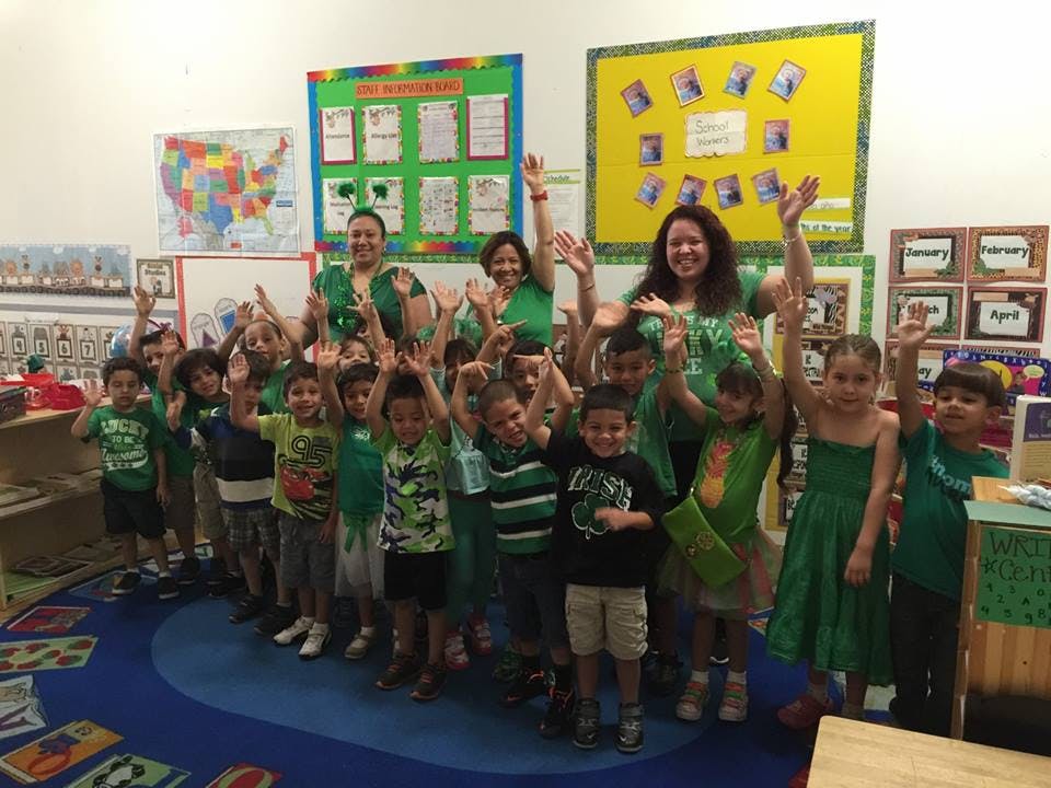 Adults and children in a classroom raising their hands