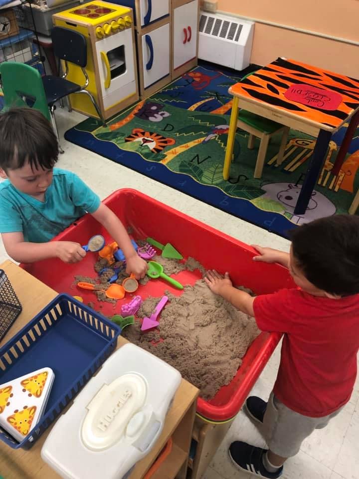 Two children playing with sand and toys in a red sand table