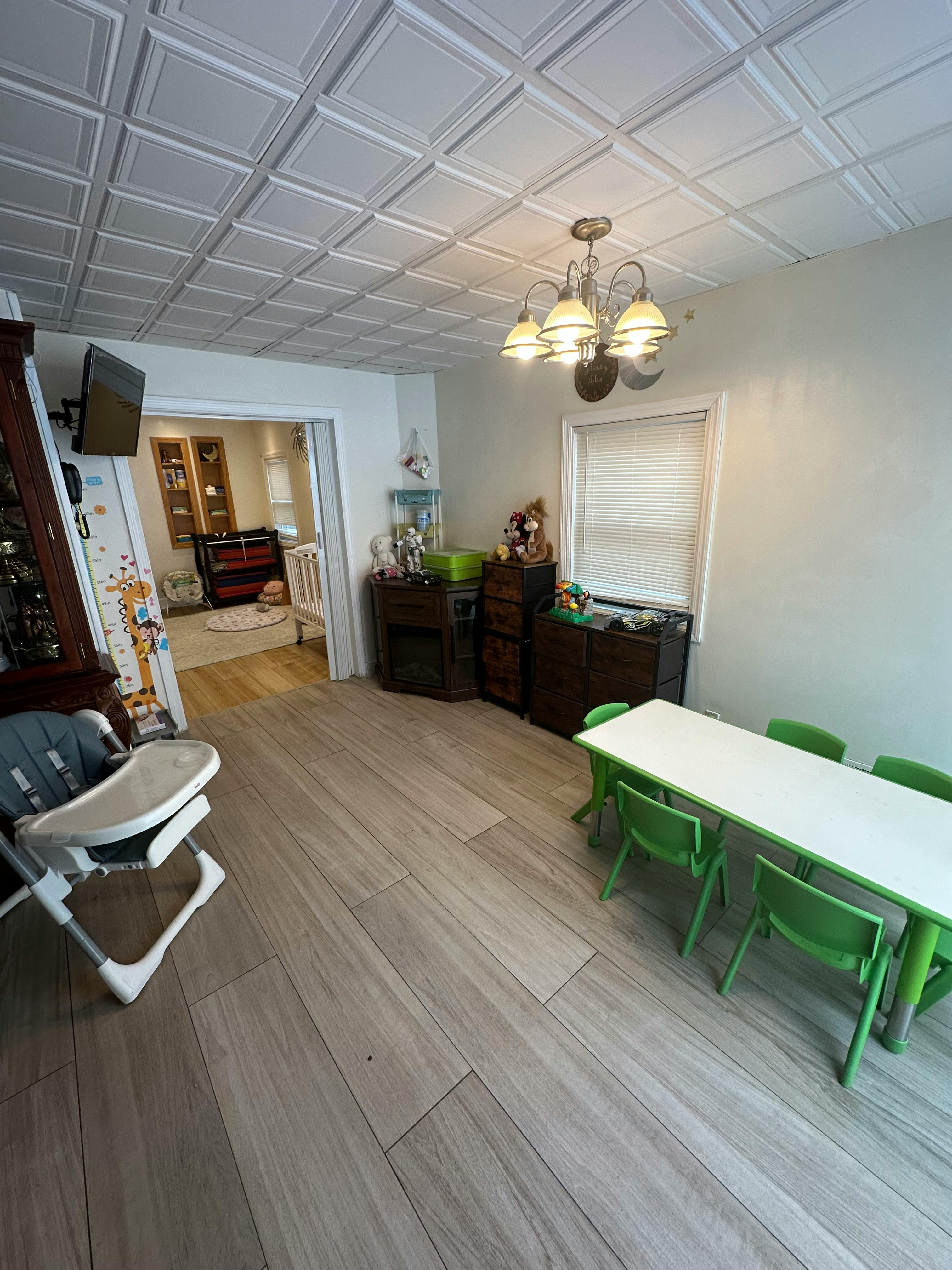 Dining room with a long table and green chairs, high chair, and chandelier