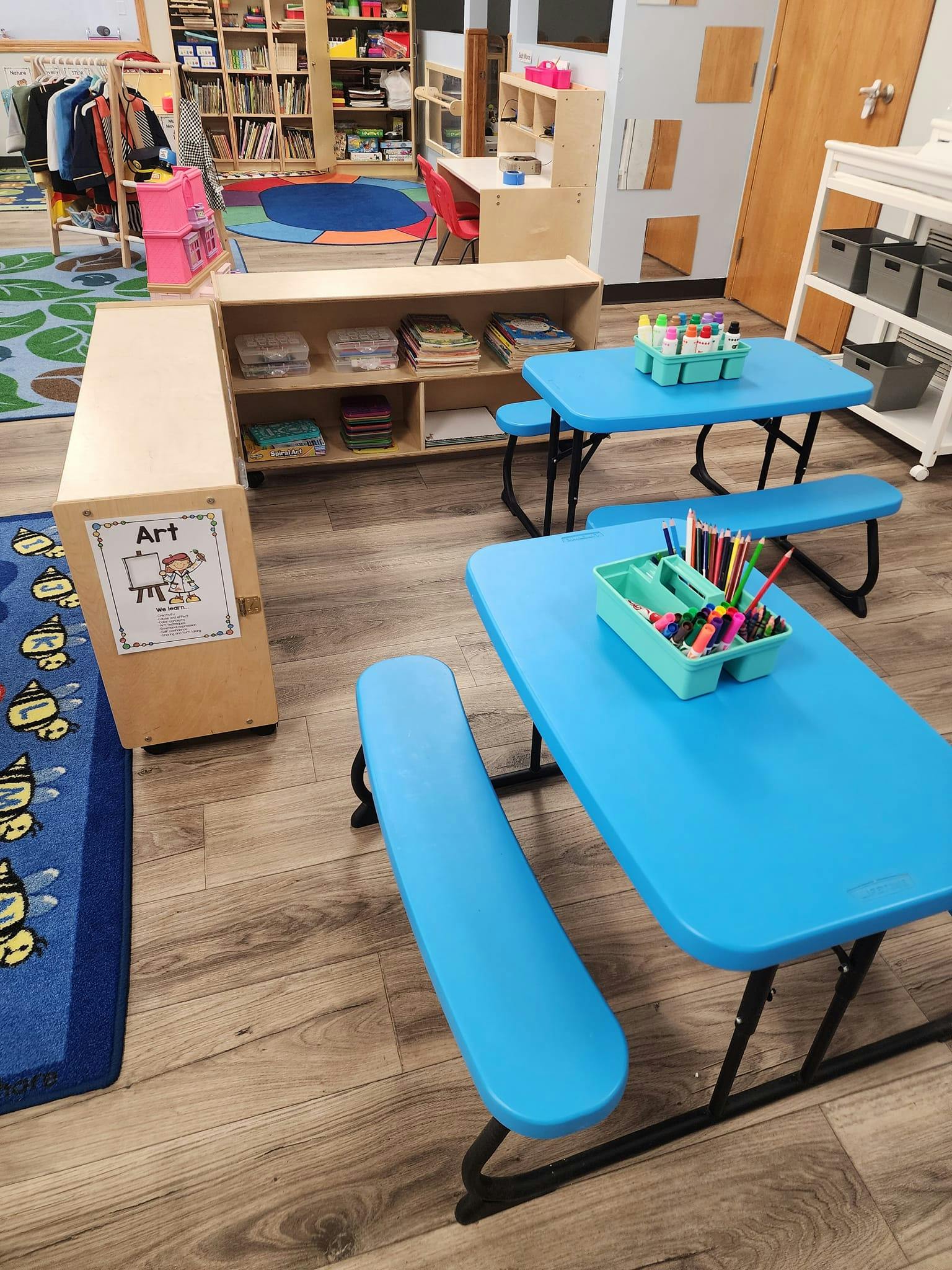 Classroom with blue tables and benches, shelves with books and supplies