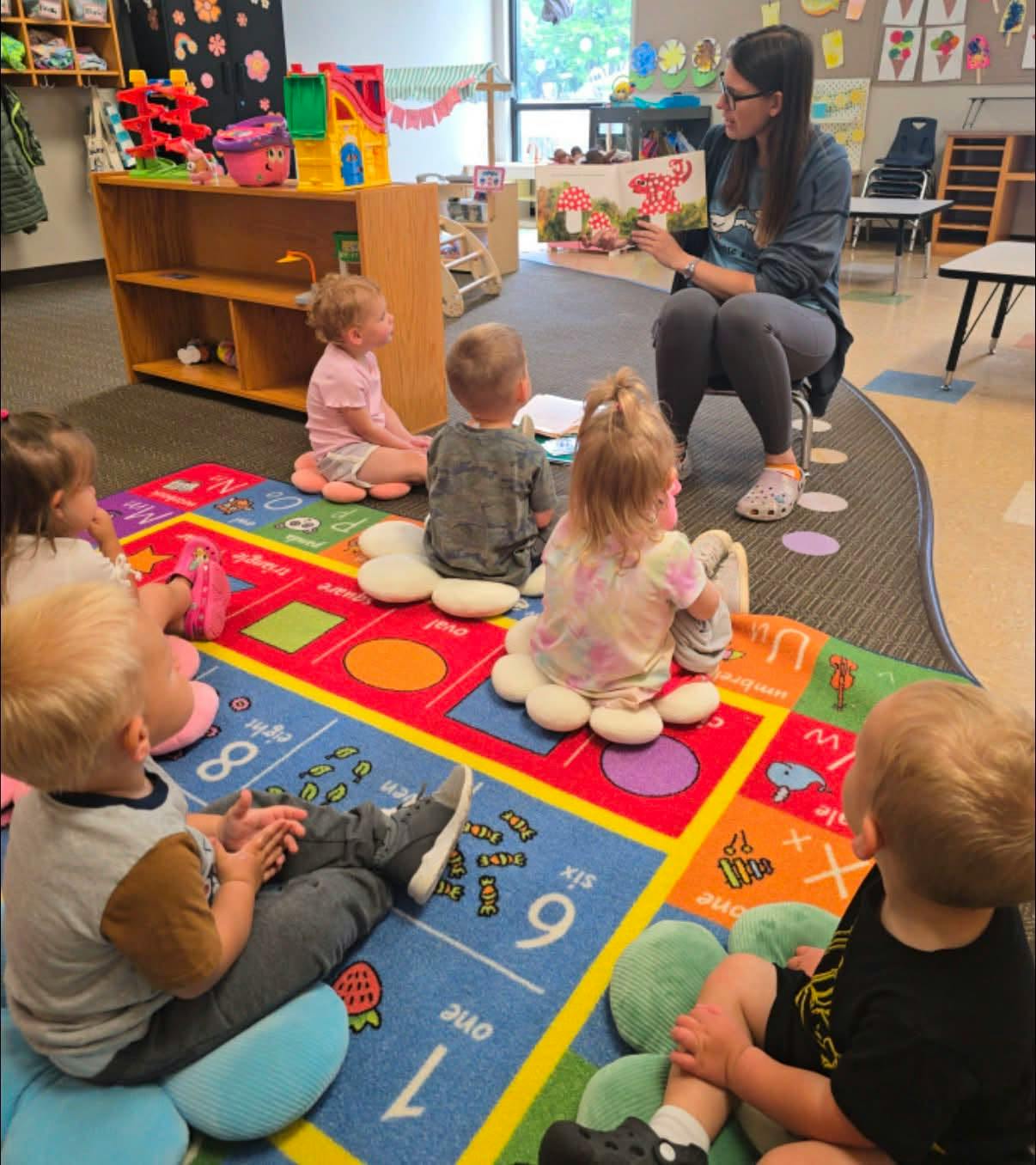 Teacher reading a book to a group of children sitting on a classroom rug