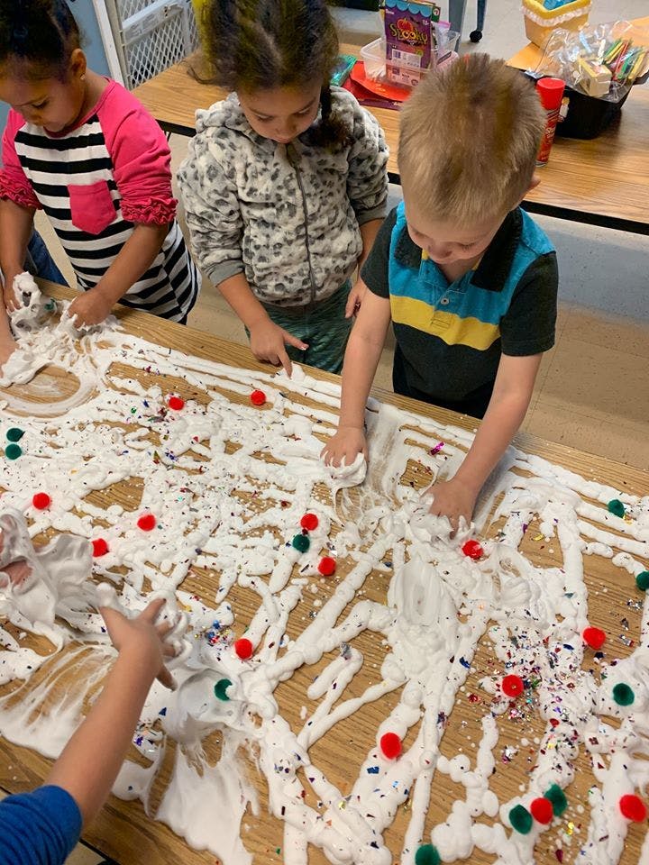 Children playing with shaving cream and pom-poms on a table