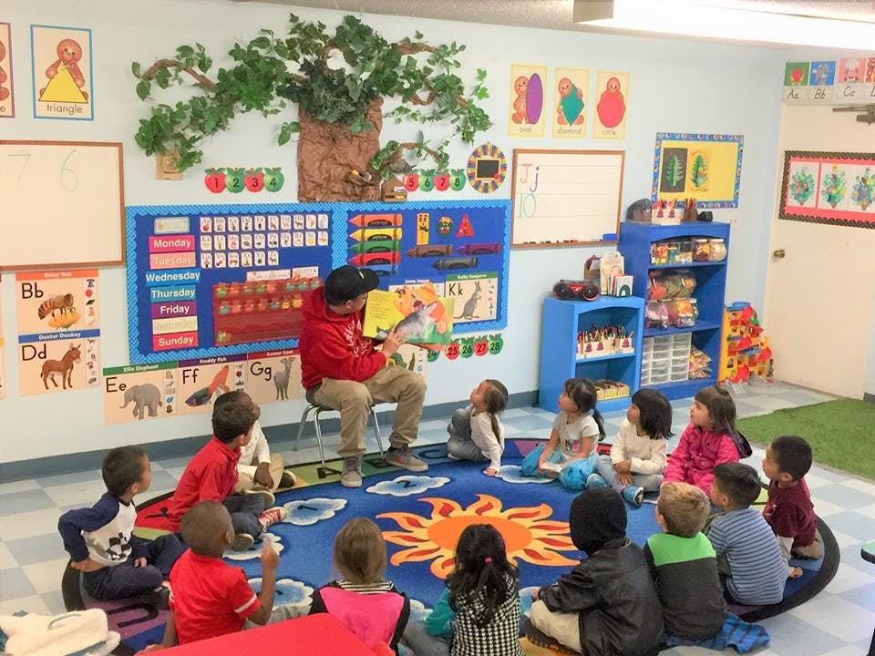 Person reading a book to a group of children in a classroom