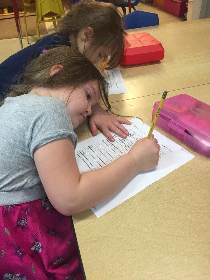 Two children writing on paper at a table