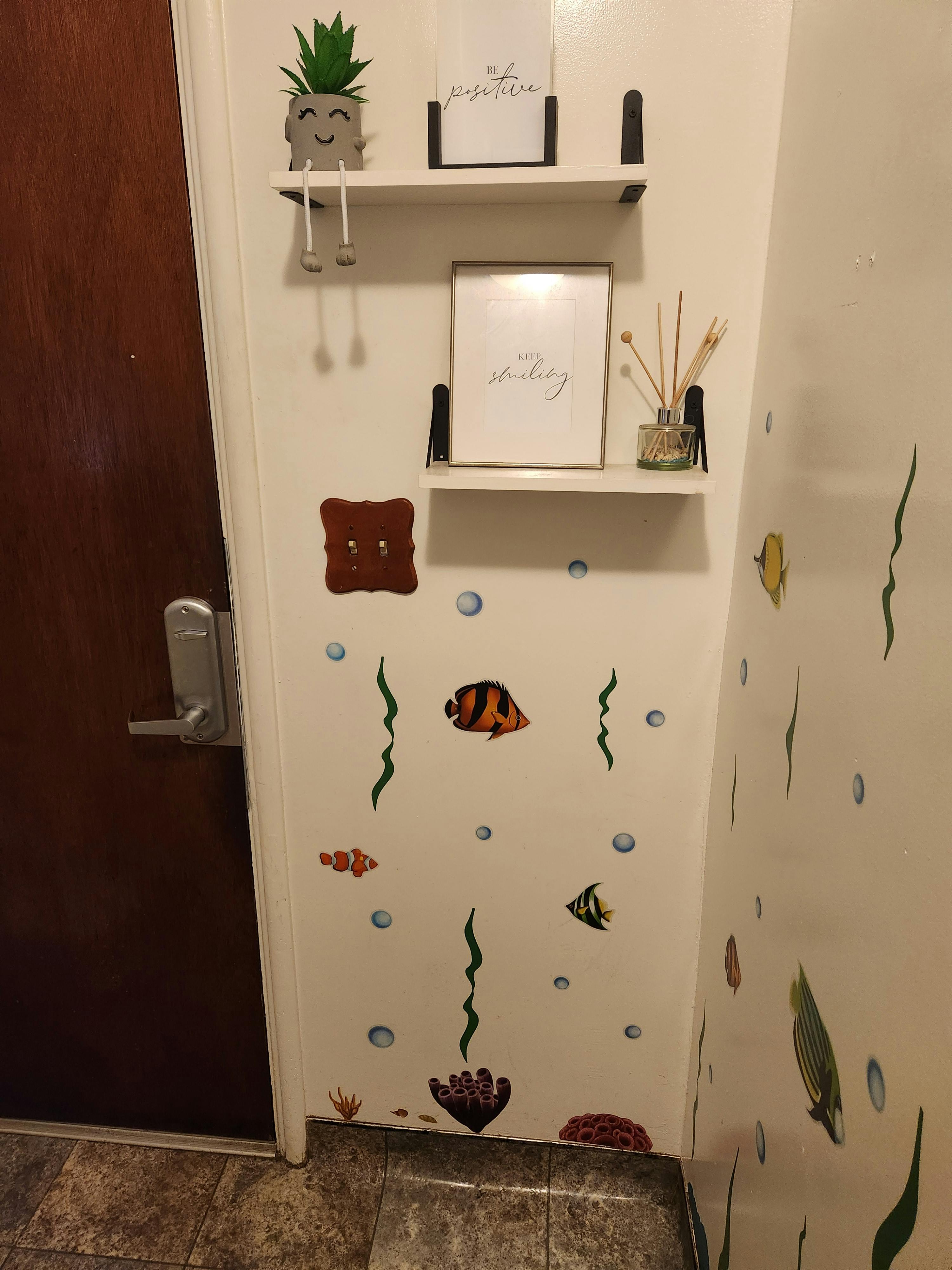 Wall with shelves, plant, and fish decals next to a door