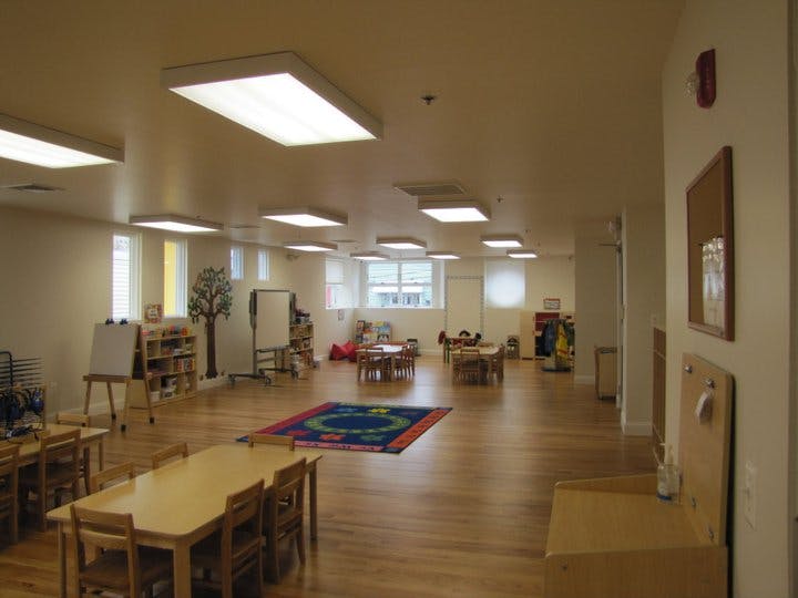 Empty classroom with small tables and chairs, and a colorful rug