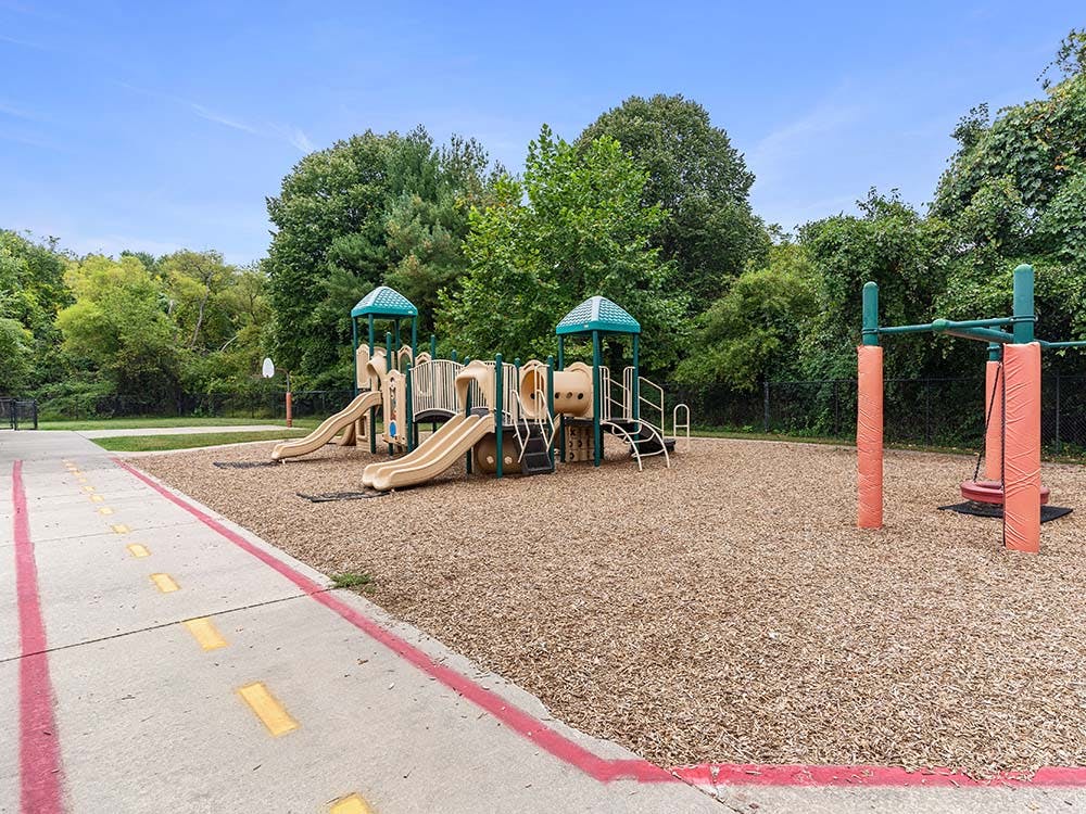 Playground with slides and monkey bars on wood chips next to a paved path
