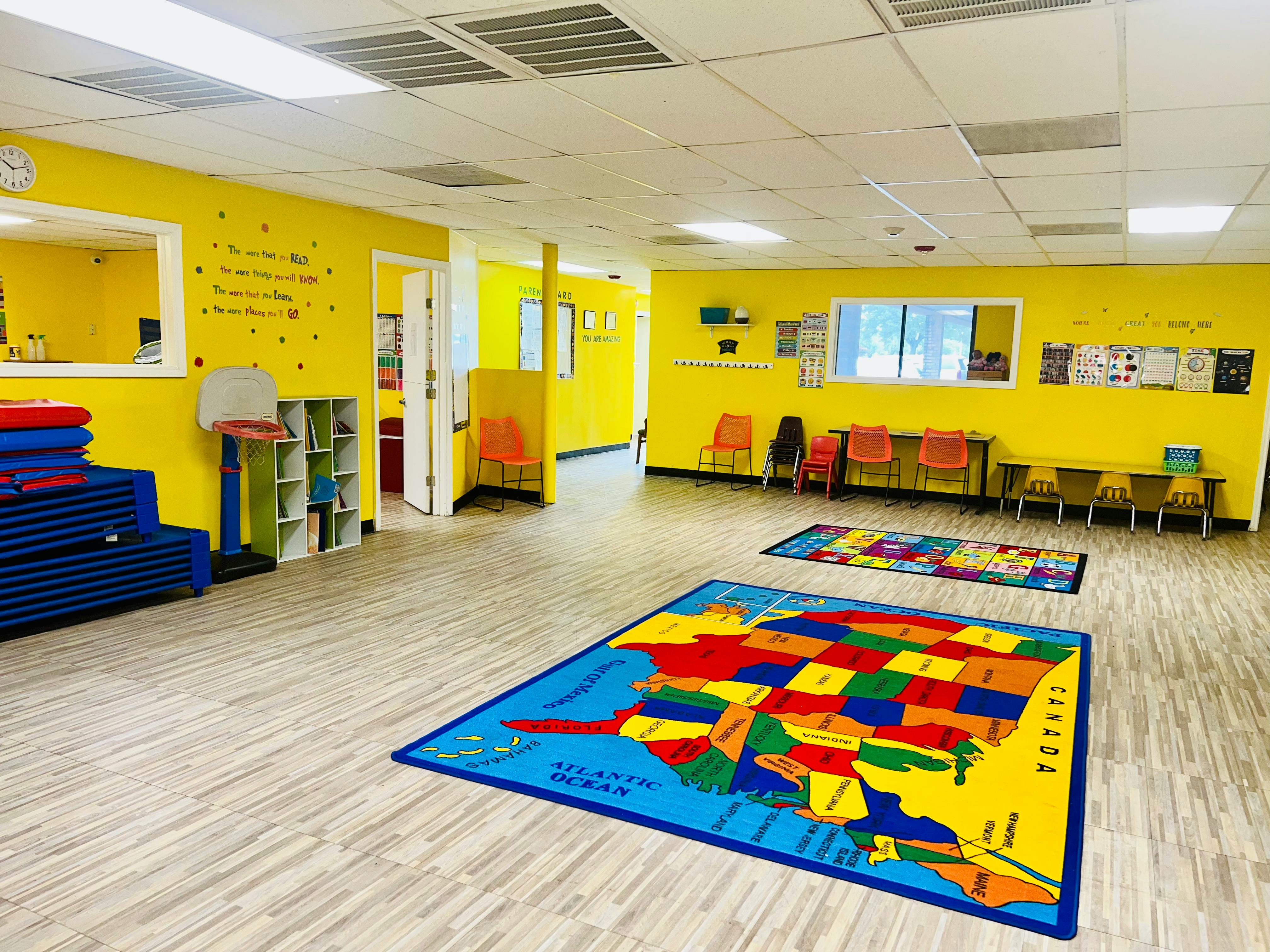 Classroom with yellow walls, map rug, and small tables with chairs