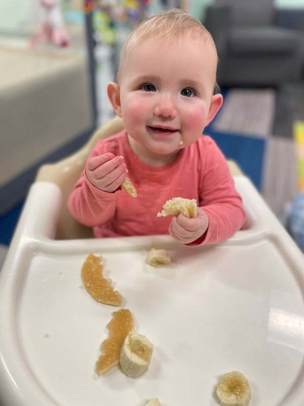 Child in a high chair holding pieces of fruit