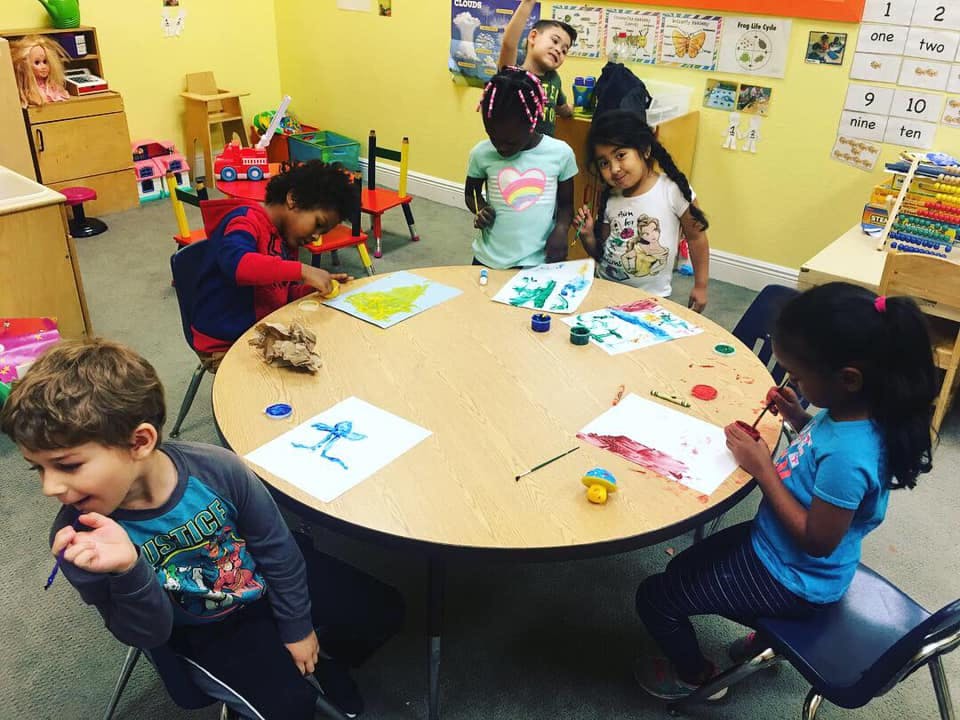 Children painting and drawing at a round table in a classroom