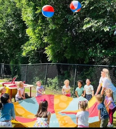 Children and an adult playing with a parachute and beach balls outdoors
