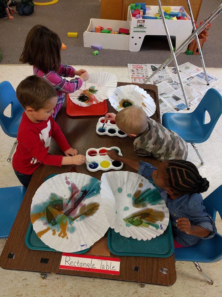 Children painting on coffee filters at a table
