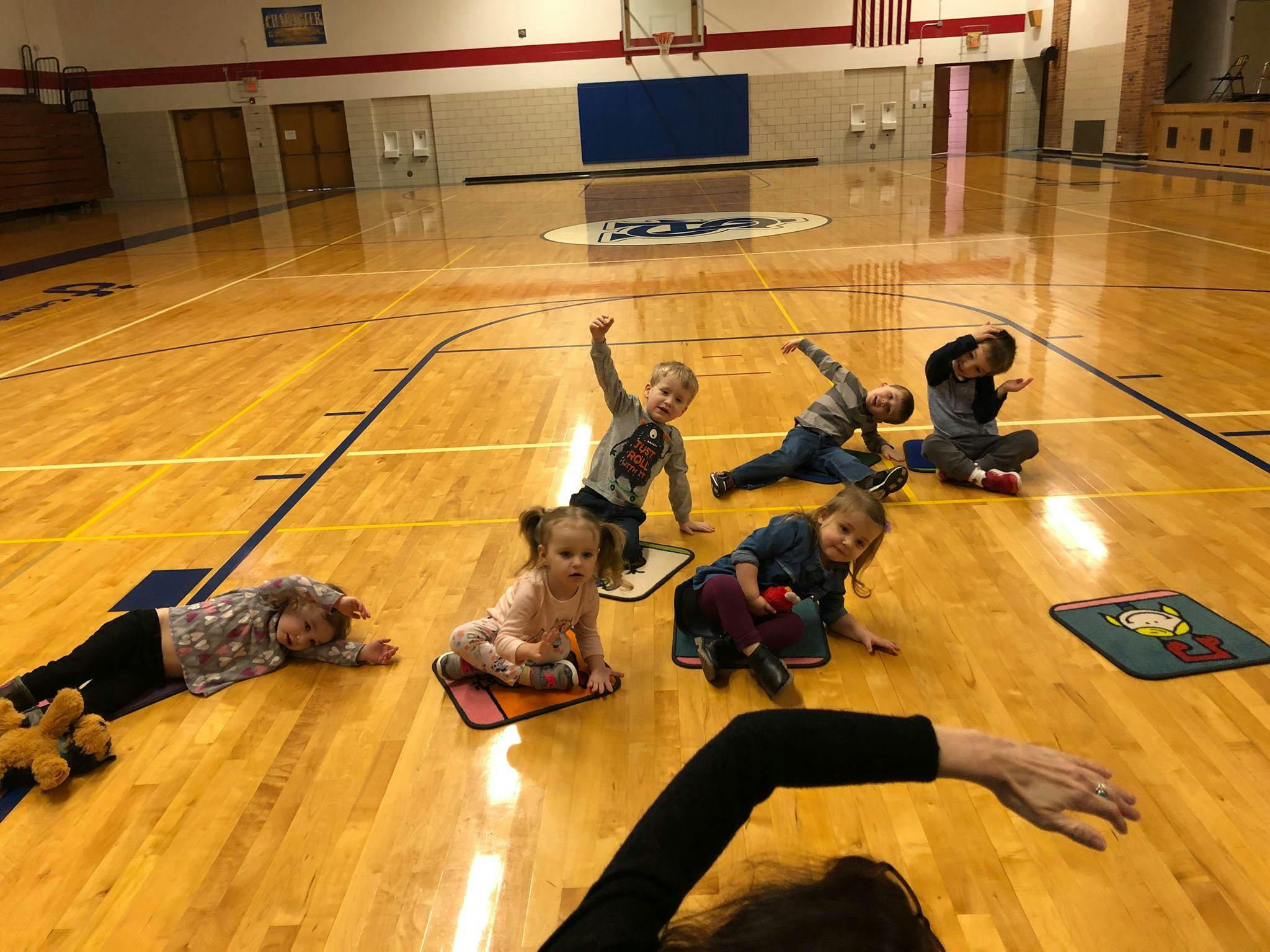 Children sitting and lying on mats on a gymnasium floor
