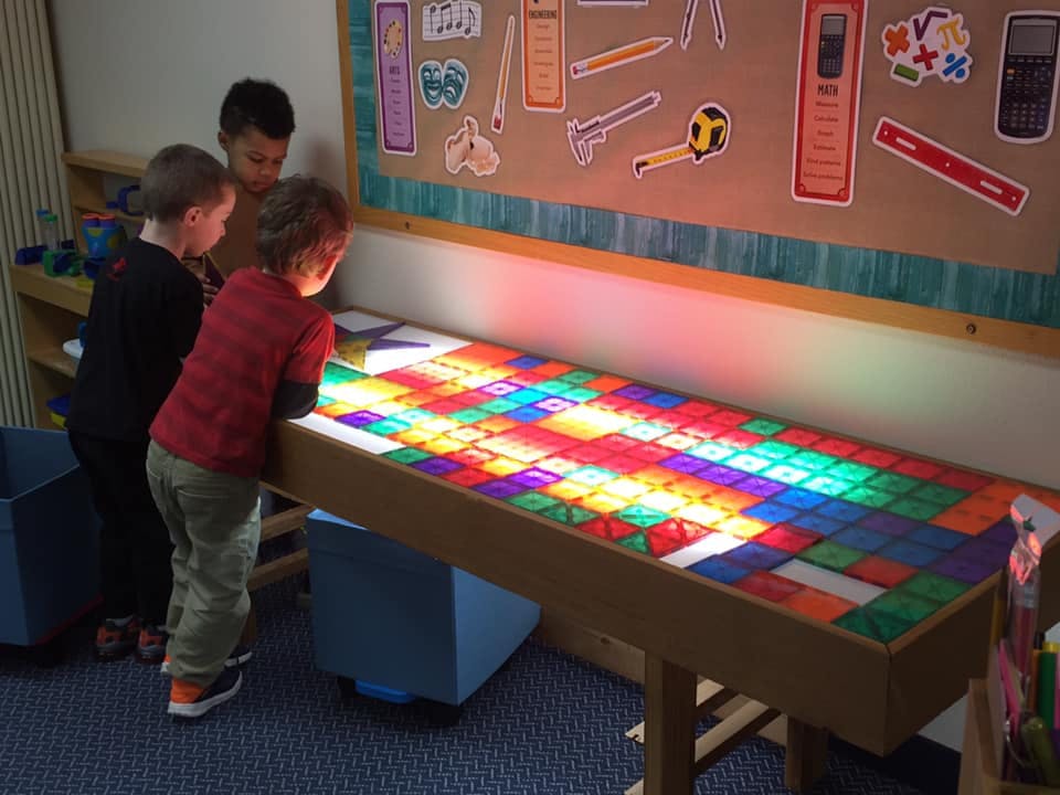 Three children looking at a light table with colorful blocks