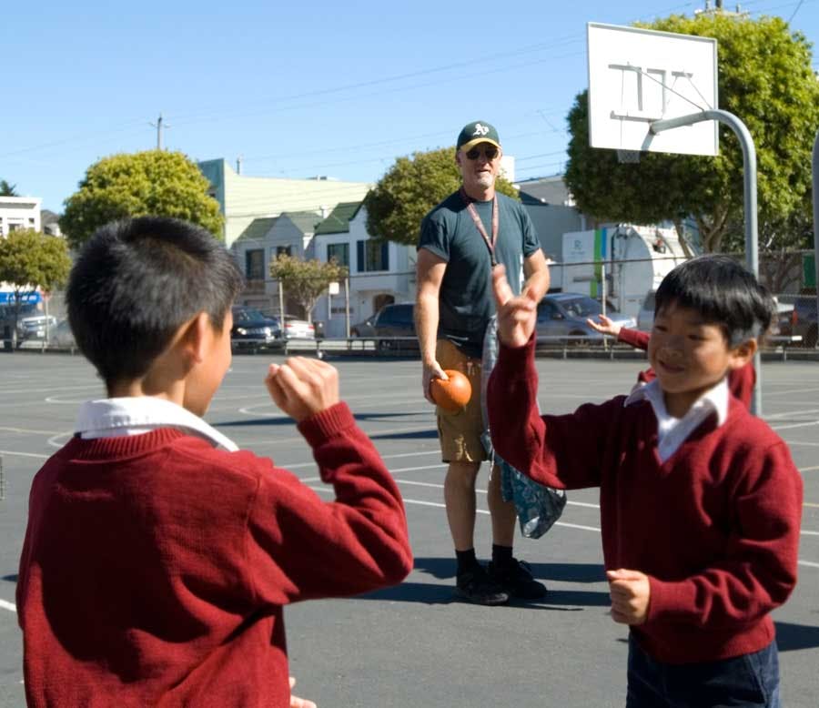Child making a peace sign on a basketball court with a person holding a ball