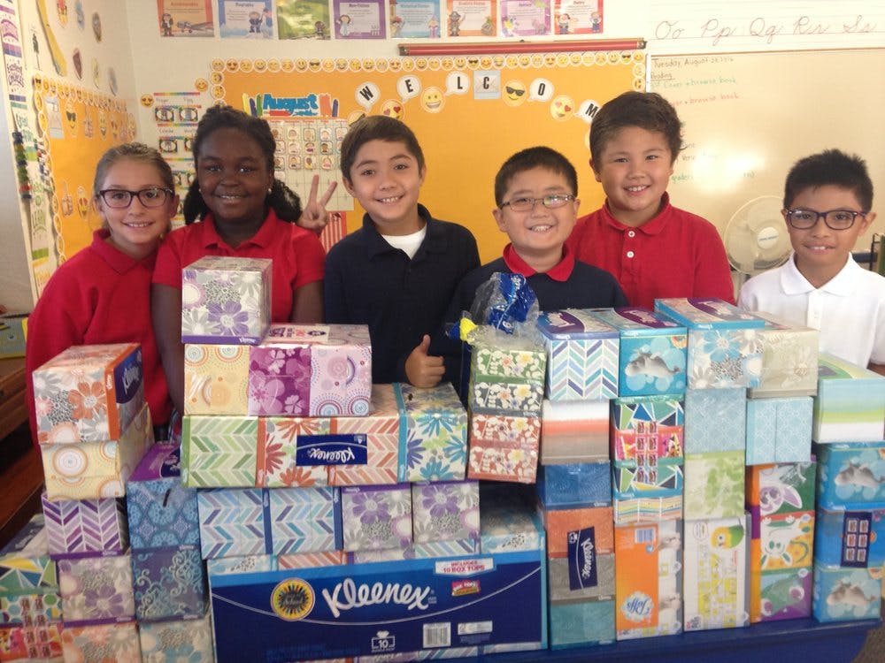 Six children standing behind a table stacked with boxes of tissues