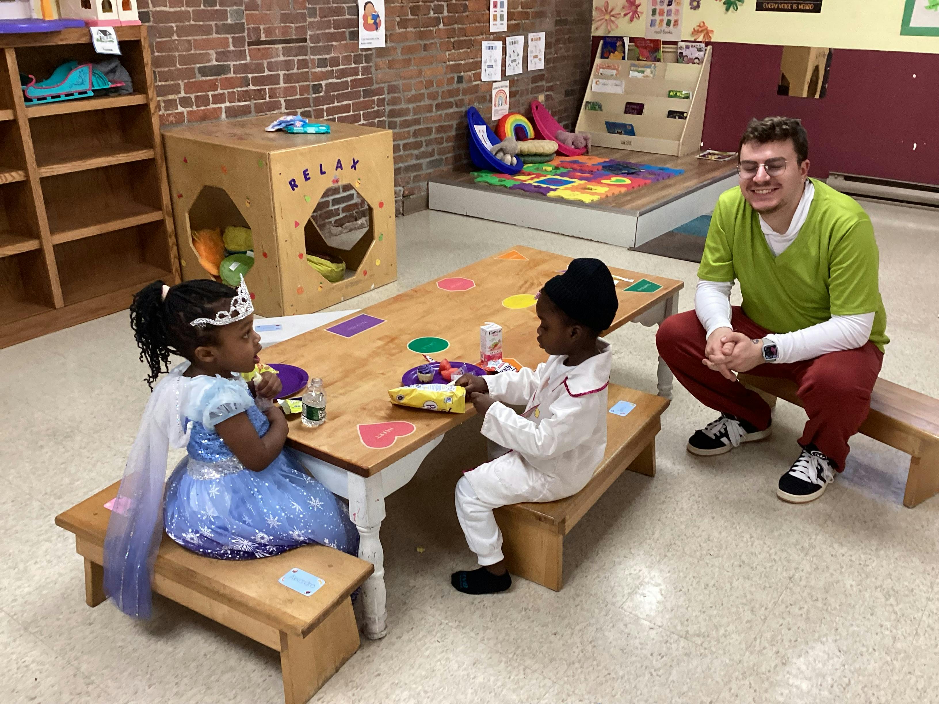 Adult and two children sitting at a table in a classroom