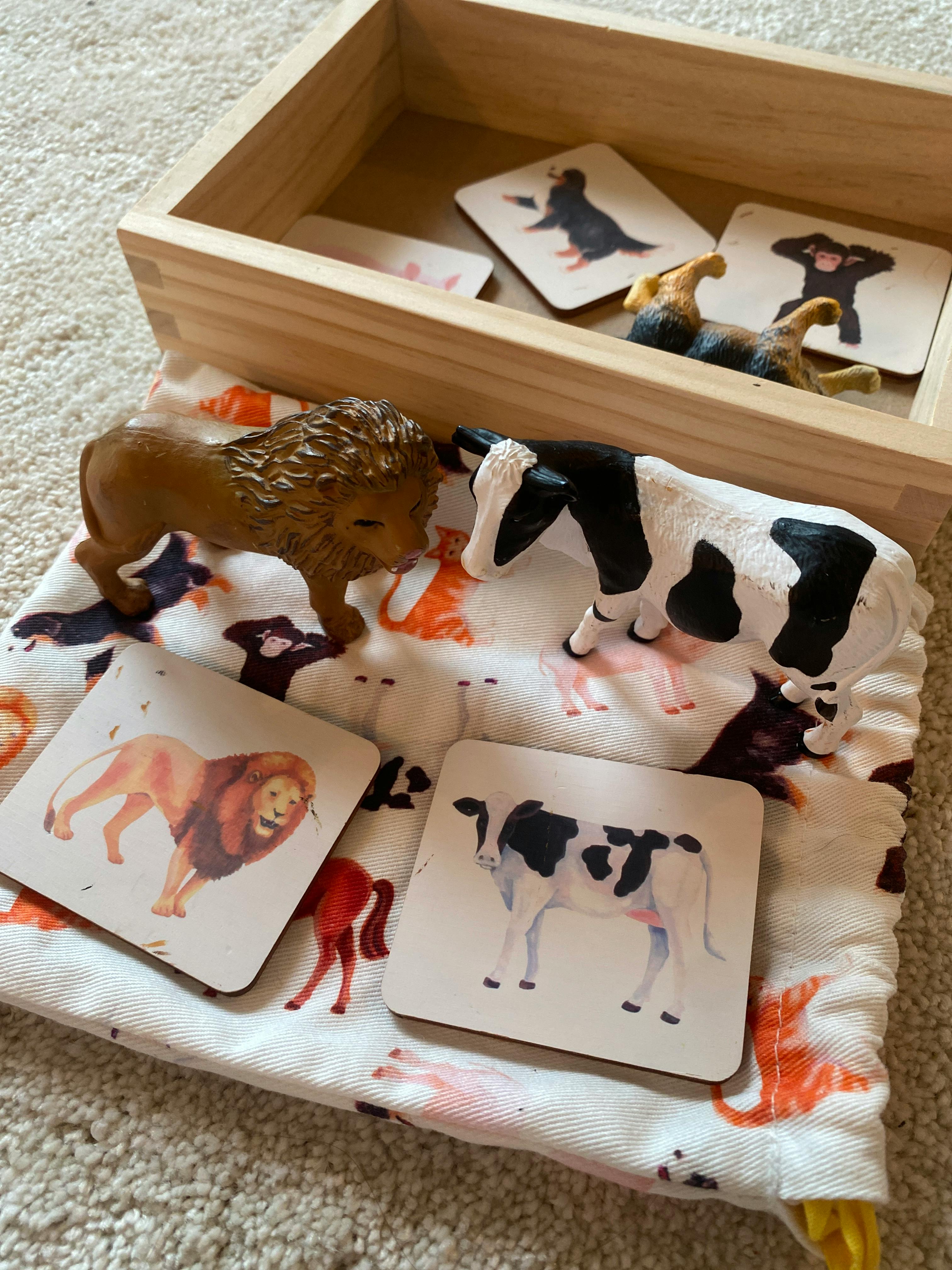Toy lion and cow with matching animal cards on a patterned cloth