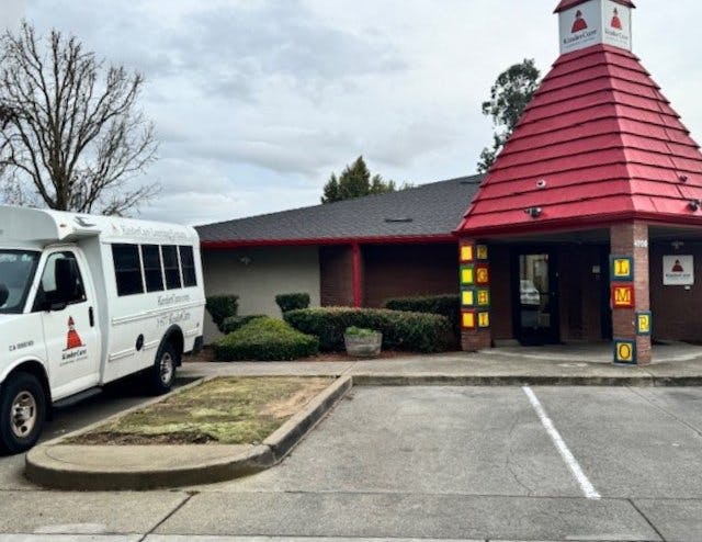 A white shuttle bus parked next to a KinderCare building
