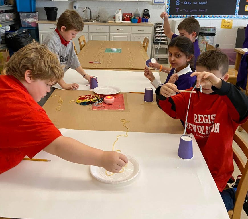 Children doing an activity with string and cups at a table