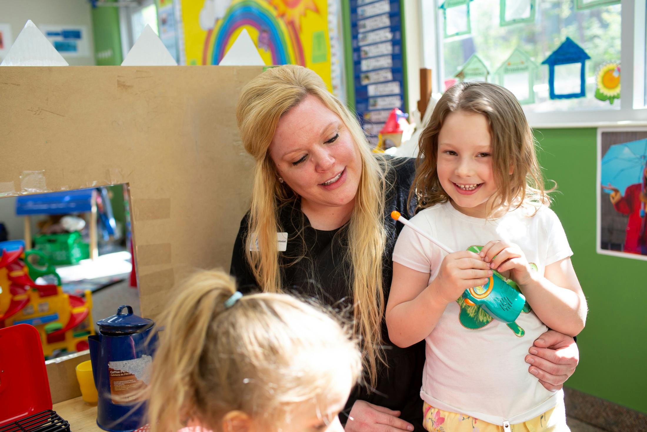 Person with long hair holding a child in a classroom